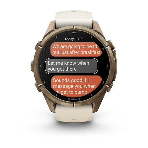A Garmin smartwatch with a round bronze-toned case and a light beige silicone strap, shown on a clean white background. The watch face displays a messaging app screen.