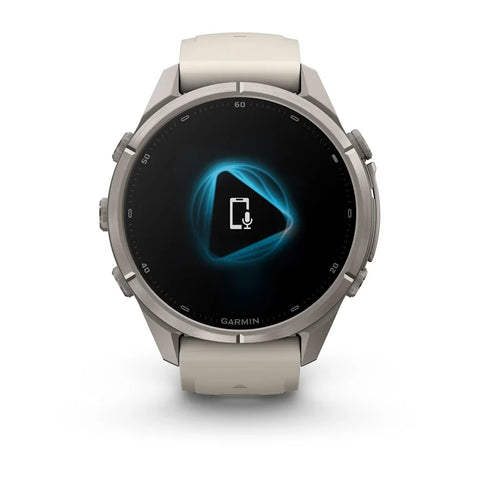A Garmin smartwatch with a round silver-toned metal case and a light beige silicone strap, shown against a plain white background. The watch face displays a black screen with a glowing blue geometric icon.