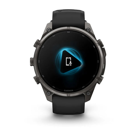 A Garmin smartwatch with a dark gray metallic case and a black strap, shown from the front on a clean white background. The watch face displays a black screen with a glowing blue geometric icon.