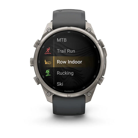 A Garmin smartwatch with a dark gray strap and a silver-toned metal case, displaying a fitness menu on its screen against a white background.