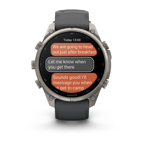 A Garmin smartwatch with a dark gray strap and a silver-toned metal case, shown on a clean white background. The watch face displays a messaging app with orange and gray message bubbles.