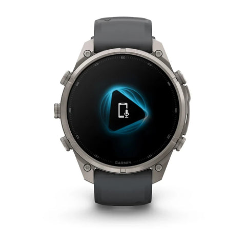 A Garmin smartwatch with a round silver-toned metal case and a dark gray silicone strap, shown against a plain white background. The watch face displays a black screen with a glowing blue geometric icon.