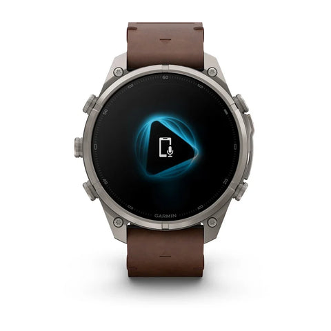 A Garmin smartwatch with a brown leather strap and a silver-toned metal case, shown against a plain white background. The watch face displays a black screen with a glowing blue geometric icon.