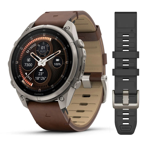 A Garmin smartwatch with a brown leather strap shown alongside an additional black silicone strap on a clean white background.