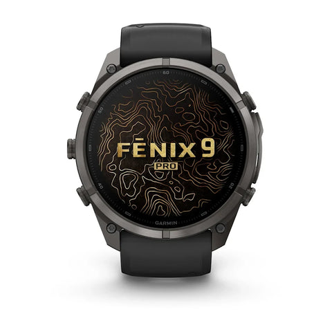 A Garmin Fenix 9 Pro smartwatch with a dark gray metallic case and a black strap, shown from the front on a white background. The watch face displays a black background with gold topographic lines and the text 'FENIX 9 PRO'.