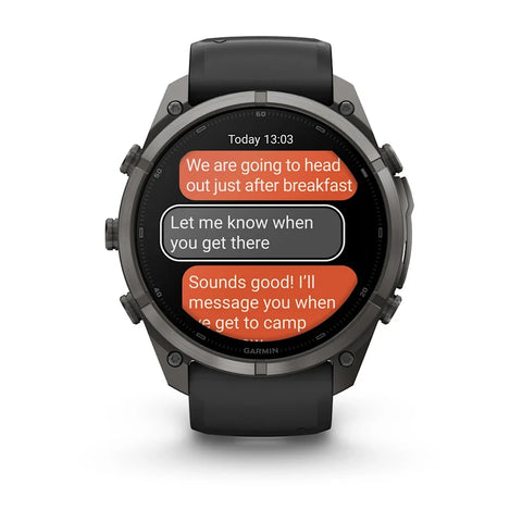 A Garmin smartwatch with a black case and black strap, shown from the front on a white background. The screen displays a messaging app with orange and gray text bubbles.