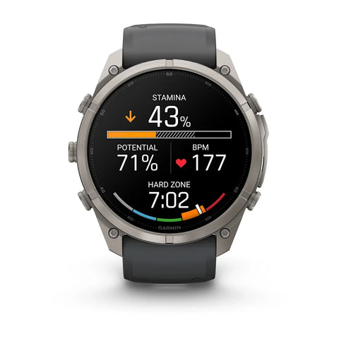 A Garmin smartwatch with a round silver-tone metal case and a dark gray silicone strap, shown on a clean white background. The watch face is active with various fitness and heart rate metrics displayed.