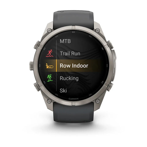 A Garmin smartwatch with a dark gray strap and a silver-toned metal case, displaying a fitness menu on its screen against a white background.