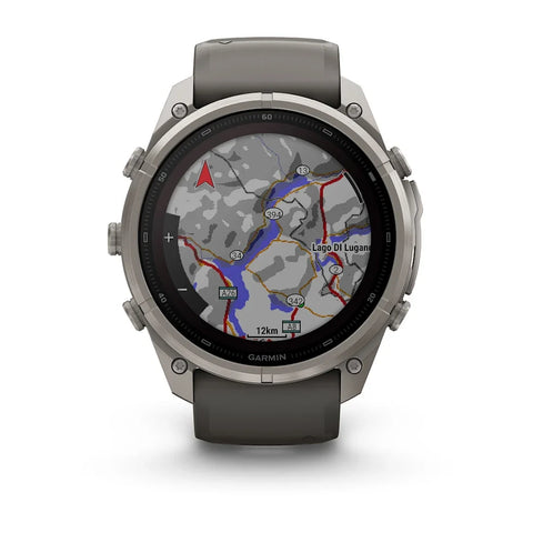 A rugged Garmin smartwatch with a round silver-tone metal case and a dark gray silicone strap, shown on a clean white background. The watch face is active with a topographic map display.