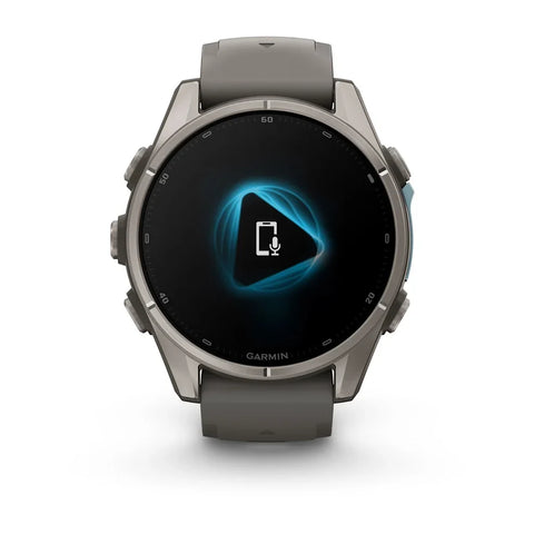 A Garmin smartwatch with a round metallic gray case and a dark gray strap, shown against a plain white background. The watch face displays a black screen with a glowing blue geometric icon and a white microphone symbol.