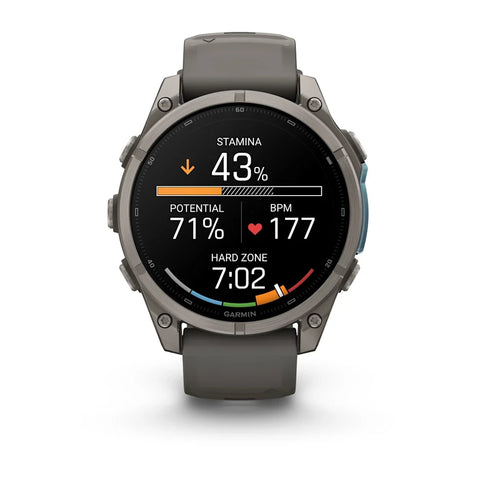 A Garmin smartwatch with a dark gray silicone strap and a metallic gray round case, shown on a clean white background. The watch face is active with various fitness and heart rate metrics displayed.