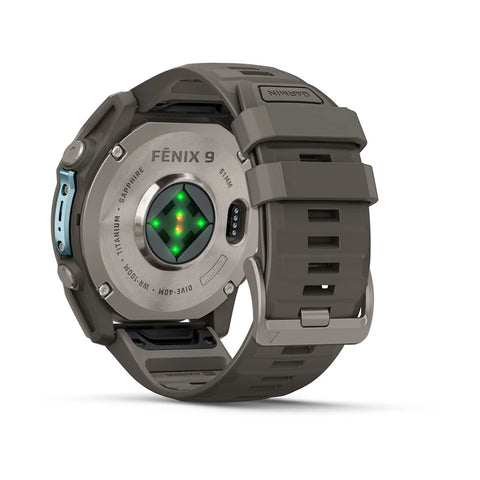 A rugged smartwatch shown from the back on a clean white background, featuring a dark gray resin strap and case with a metallic silver titanium backplate. The backplate displays 'FENIX 9' and 'SAMSUNG' along with a green LED heart rate sensor.