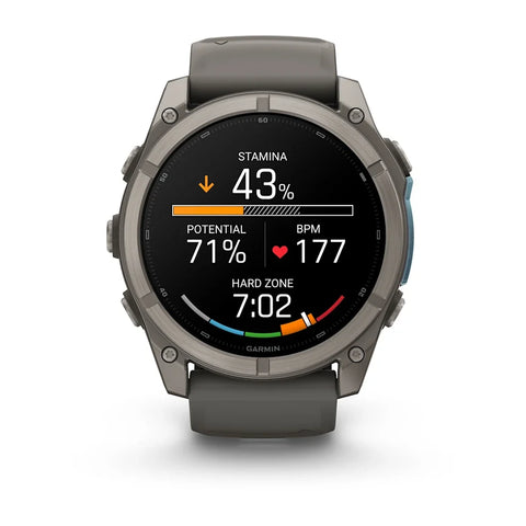 A Garmin smartwatch with a dark gray metallic case and a dark gray strap, shown on a clean white background. The watch face is active with various fitness and heart rate metrics displayed.