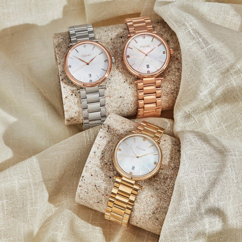 Three watches with metallic bands on textured stone and fabric background