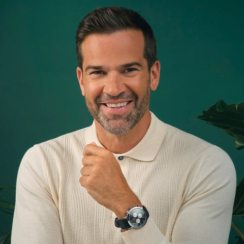 Man wearing a beige sweater and watch against a green background
