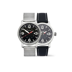 Two analog wristwatches with black dials and silver-tone cases, shown overlapping on a white background. The front watch has a silver mesh strap, and the rear watch has a black leather strap with white stitching.