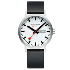 A Mondaine wrist watch with a silver-toned case, a white dial featuring black hour markers and hands, a red second hand, and a day/date window at 3 o'clock, paired with a black leather strap.