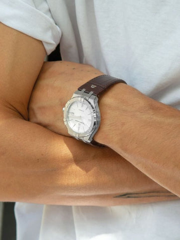 Close-up of a wrist wearing a silver watch with a brown leather strap.