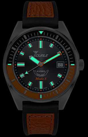 Watch with black dial, brown leather strap, and glowing green accents on a dark background