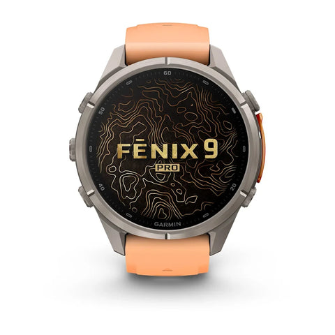 A Garmin Fenix 9 Pro smartwatch with a round silver-toned metal case, a black display screen featuring gold topographic lines and 'FENIX 9 PRO' text, and an orange silicone strap, shown on a clean white background.