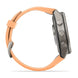 A smartwatch shown from the side profile with a dark gray metallic case and a peach-colored strap on a clean white background.