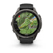 A Garmin smartwatch with a round dark gray metallic case and a black strap, shown from the front on a white background. The screen displays a green topographic map.