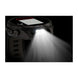 A rugged black smartwatch or headlamp-style device with a visible solar panel on the top and a bright front light turned on, casting a beam of light downward against a black background.