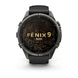 A Garmin Fenix 9 Pro smartwatch with a dark gray titanium case, black strap, and a black watch face featuring gold topographic lines and the text 'FENIX 9 PRO'.