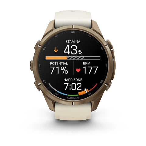 A Garmin smartwatch with a round bronze-toned case and a light beige strap, shown on a clean white background. The watch face is active with various fitness and health metrics displayed in white, orange, and red.
