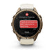 A Garmin smartwatch with a bronze-toned metal case and a light beige silicone strap, shown on a clean white background. The watch screen displays an emergency message conversation.