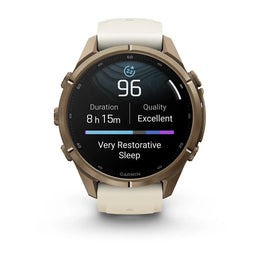 A Garmin smartwatch with a round bronze-toned metal case and a light cream-colored silicone strap, shown on a clean white background. The watch screen is active, displaying sleep and heart rate metrics.