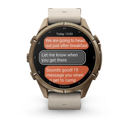 A Garmin smartwatch with a bronze-toned metal case and a light beige leather strap, shown on a clean white background. The watch face displays a messaging app interface with orange and gray text bubbles.