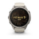 A Garmin Fenix 9 Pro smartwatch with a round silver-toned metal case, a light beige silicone strap, and a black display screen featuring gold topographic contour lines and the text 'FENIX 9 PRO'.