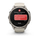 A Garmin smartwatch with a light beige/tan strap and a silver-toned metal case, shown on a clean white background. The watch screen displays an emergency message with a red SOS badge and a red reply bubble.