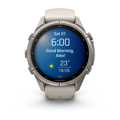 A Garmin smartwatch with a round silver stainless steel case and a light beige silicone strap, shown on a clean white background. The watch face is illuminated with a blue digital weather display.