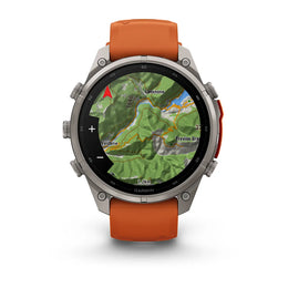 A Garmin smartwatch with a round silver-tone metal case and an orange silicone strap, shown on a clean white background. The watch face is active with a green topographic map display.