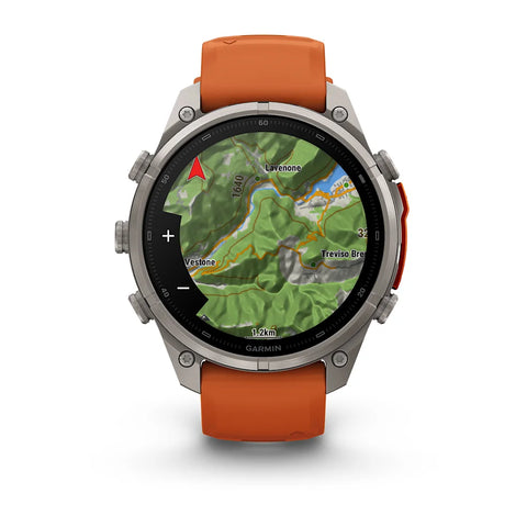A Garmin smartwatch with a round silver-tone metal case and an orange silicone strap, shown on a clean white background. The watch face is active with a green topographic map display.