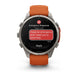 A Garmin smartwatch with a silver-toned metal case and an orange silicone strap, shown on a clean white background. The watch screen displays an emergency message interface with red and white text bubbles.