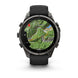 A Garmin smartwatch with a round dark gray metallic case and a black strap, shown on a clean white background. The watch face is active with a green topographic map display.