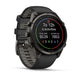A Garmin smartwatch with a dark gray and black case and a matching dark gray strap, shown at a three-quarter angle on a white background. The watch face displays fitness metrics.