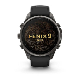 A Garmin Fenix 9 Pro smartwatch with a dark gray metallic case and a black strap, shown from the front on a white background. The watch face displays a black background with gold topographic contour lines and the text 'FENIX 9 PRO'.