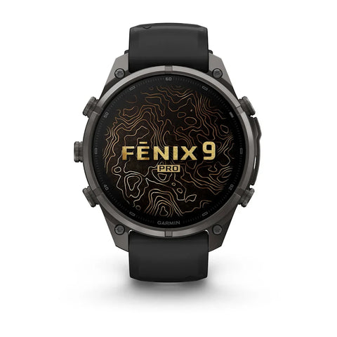 A Garmin Fenix 9 Pro smartwatch with a dark gray metallic case and a black strap, shown from the front on a white background. The watch face displays a black background with gold topographic contour lines and the text 'FENIX 9 PRO'.