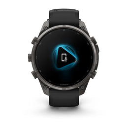A Garmin smartwatch with a dark gray metallic case and a black strap, shown from the front on a clean white background. The watch face displays a black screen with a glowing blue geometric icon.
