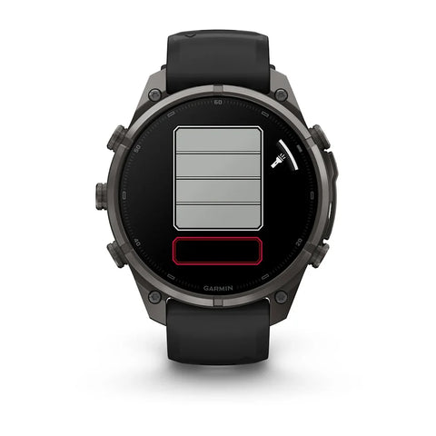 A Garmin smartwatch with a dark gray metallic case and a black strap, shown from the front on a white background. The watch face displays a digital battery indicator graphic with gray and red sections.