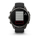 A Garmin smartwatch with a dark gray metallic case and a black strap, shown from the front on a white background. The watch face displays a digital battery indicator graphic with gray and red sections.