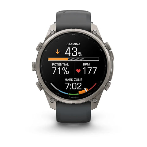 A Garmin smartwatch with a round silver-tone metal case and a dark gray silicone strap, shown on a clean white background. The watch face is active with various fitness and heart rate metrics displayed.