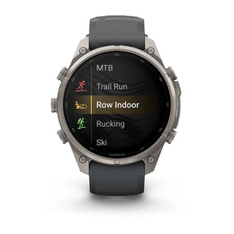 A Garmin smartwatch with a dark gray strap and a silver-toned metal case, displaying a fitness menu on its screen against a white background.