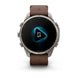 A Garmin smartwatch with a brown leather strap and a silver-toned metal case, shown against a plain white background. The watch face displays a black screen with a glowing blue geometric icon.