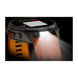A rugged smartwatch with a dark gray case and an orange strap, shown with a bright built-in flashlight illuminated on a black background.