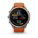 A Garmin smartwatch with a silver-toned metal case and an orange silicone strap, shown against a plain white background. The watch face is active with various fitness and heart rate metrics displayed.